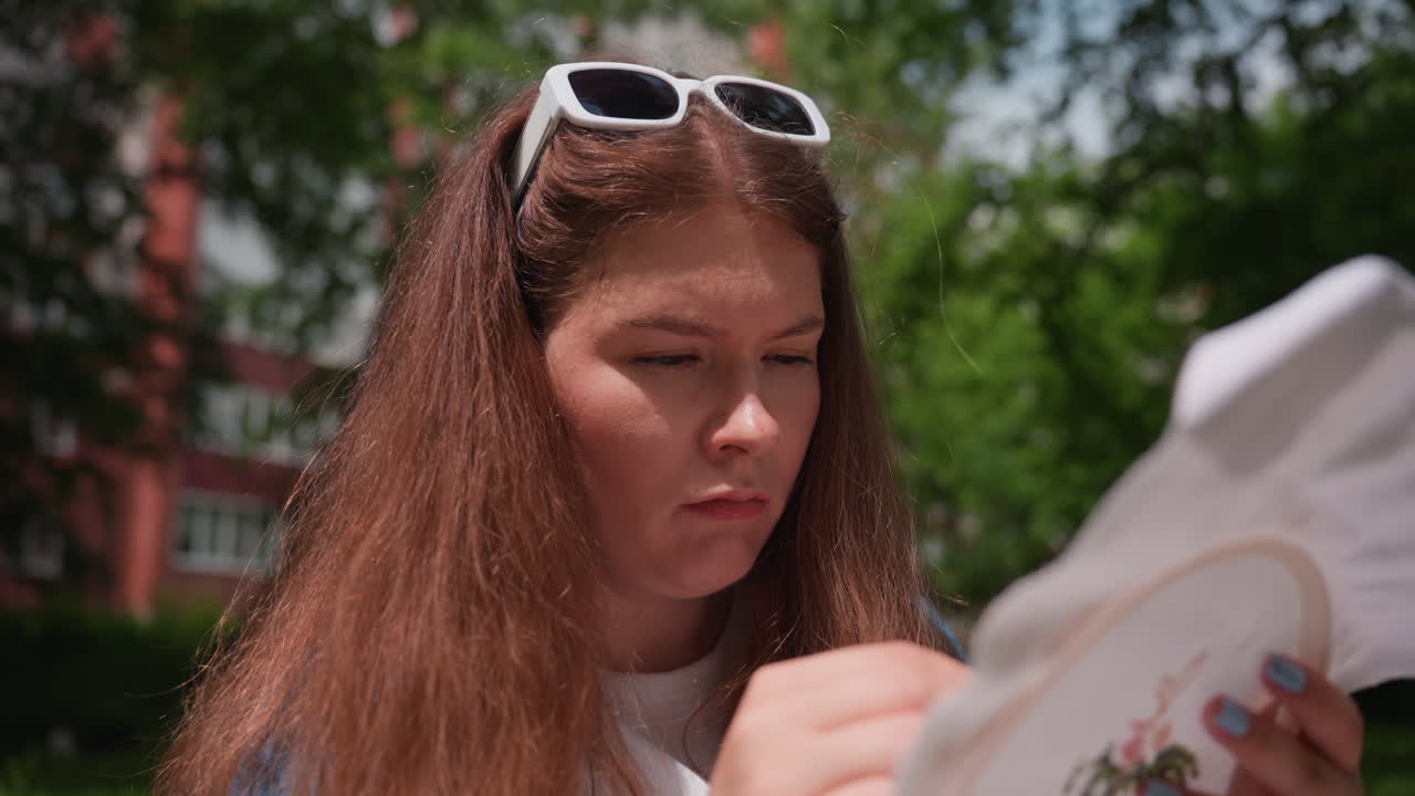 Close up of young designer working carefully on embroidery hoop during sunny outdoor day, creating delicate floral pattern on fabric, showing patience, focus, and artistic dedication in natural light