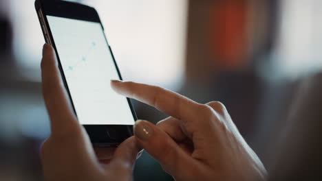 Close-up-of-womans-hands-using-smart-phone-to-read-business-graphs