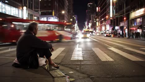 a man sits alone on a street corner in a bustling city, surrounded by fast-moving traffic and bright city lights, showcasing the contrast between urban vibrancy and solitude.