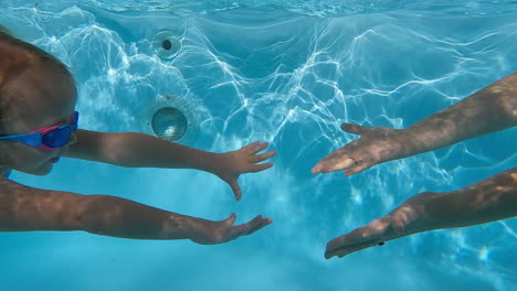 la niña y la madre se tocan las manos bajo el agua.