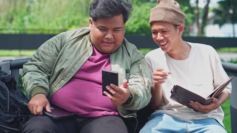 two asian young college student using smartphone together while sitting on bench at park