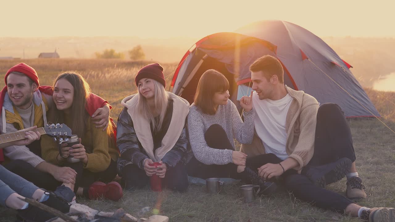 счастливые друзья отдыхают, слушая гитару на костре в лагере