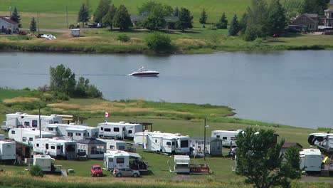 A-speedboat-slowly-goes-up-the-Bouctouche-River-near-some-trailers-on-the-shore-near-Sainte-Marie-de-Kent-in-New-Brunswick,-Canada