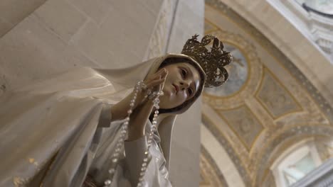 Statue-of-the-Virgin-Mary-with-a-golden-crown-and-rosary,-set-against-a-backdrop-of-an-ornate-church-interior