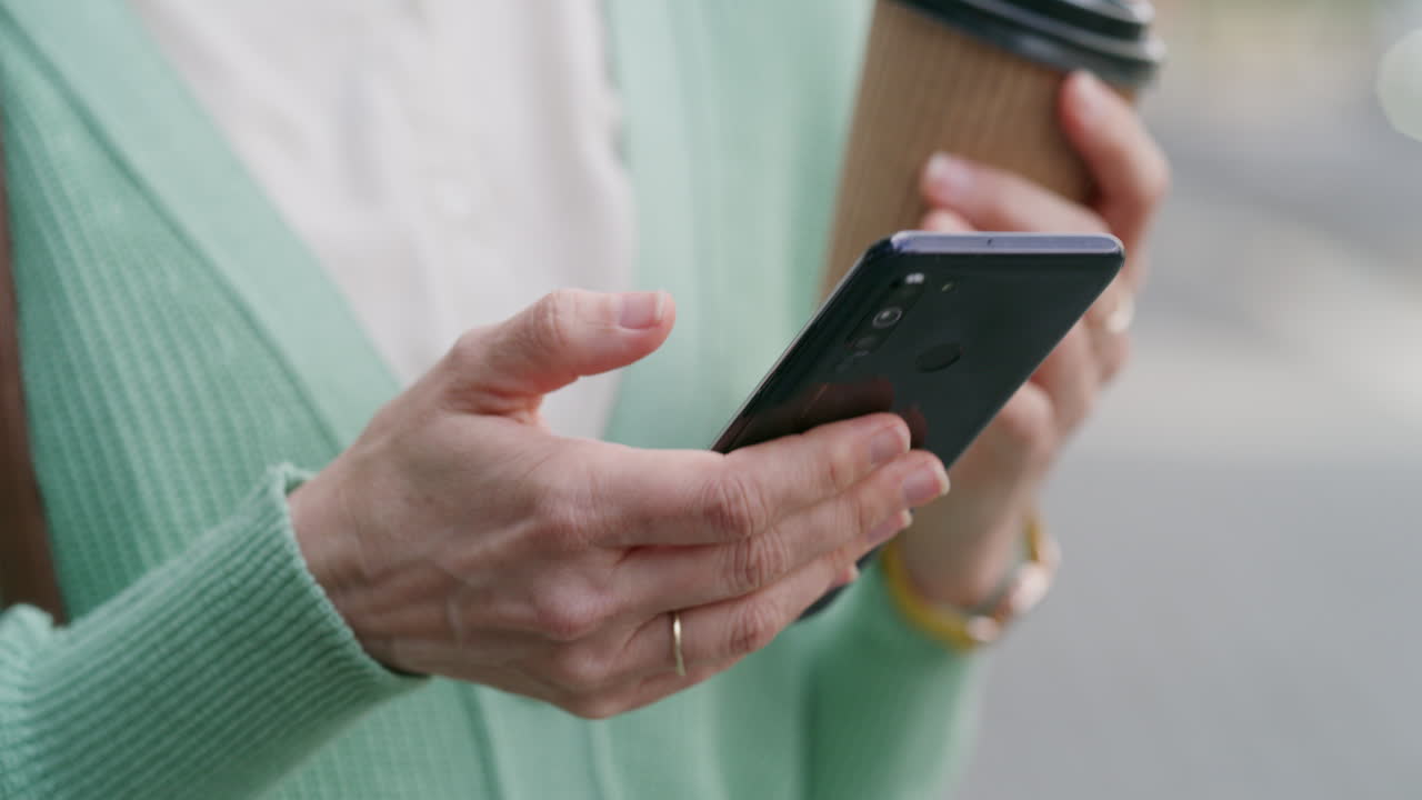 Woman using her mobile phone while holding coffee
