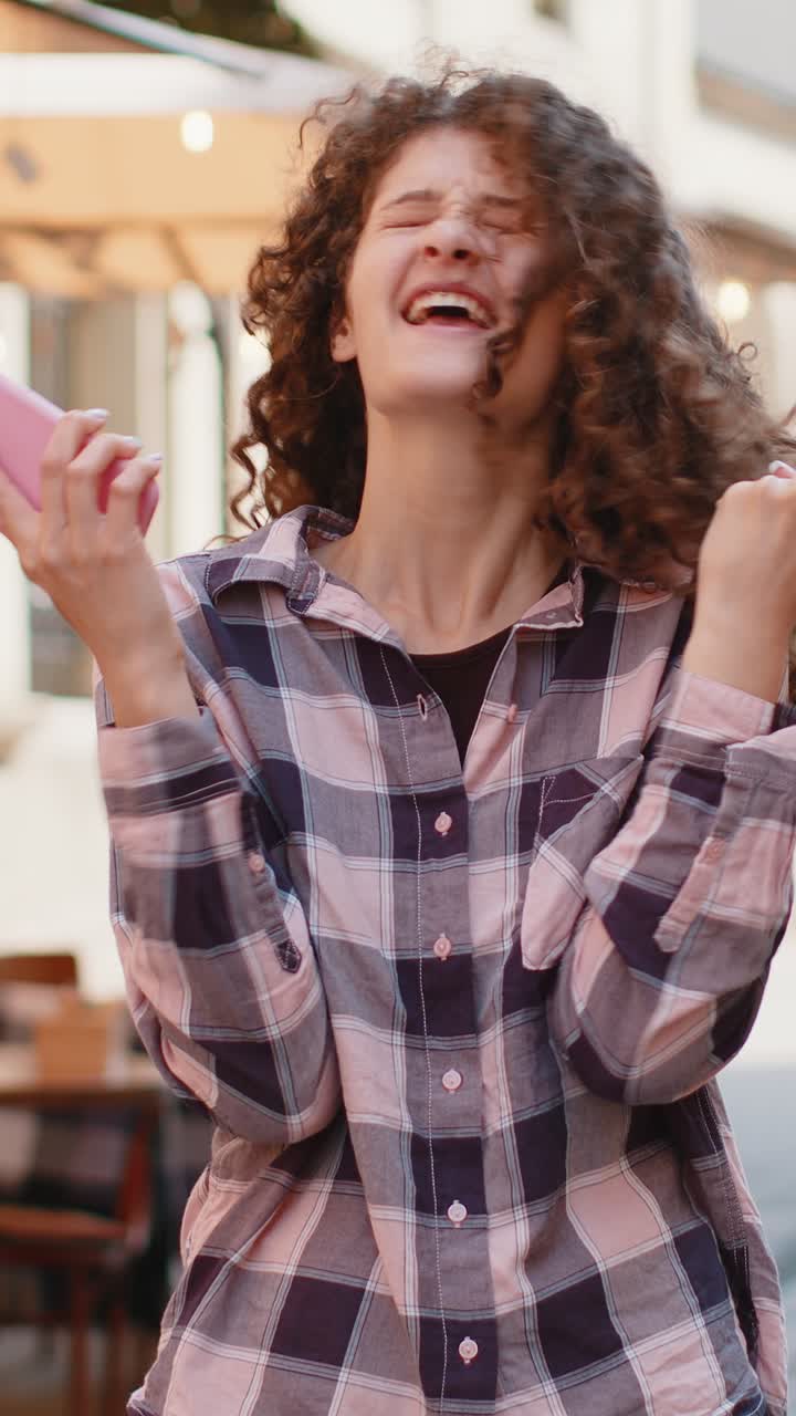 Una bella donna usa uno smartphone mobile per festeggiare la vittoria con un buon messaggio di notizie all'aperto in una strada della città urbana