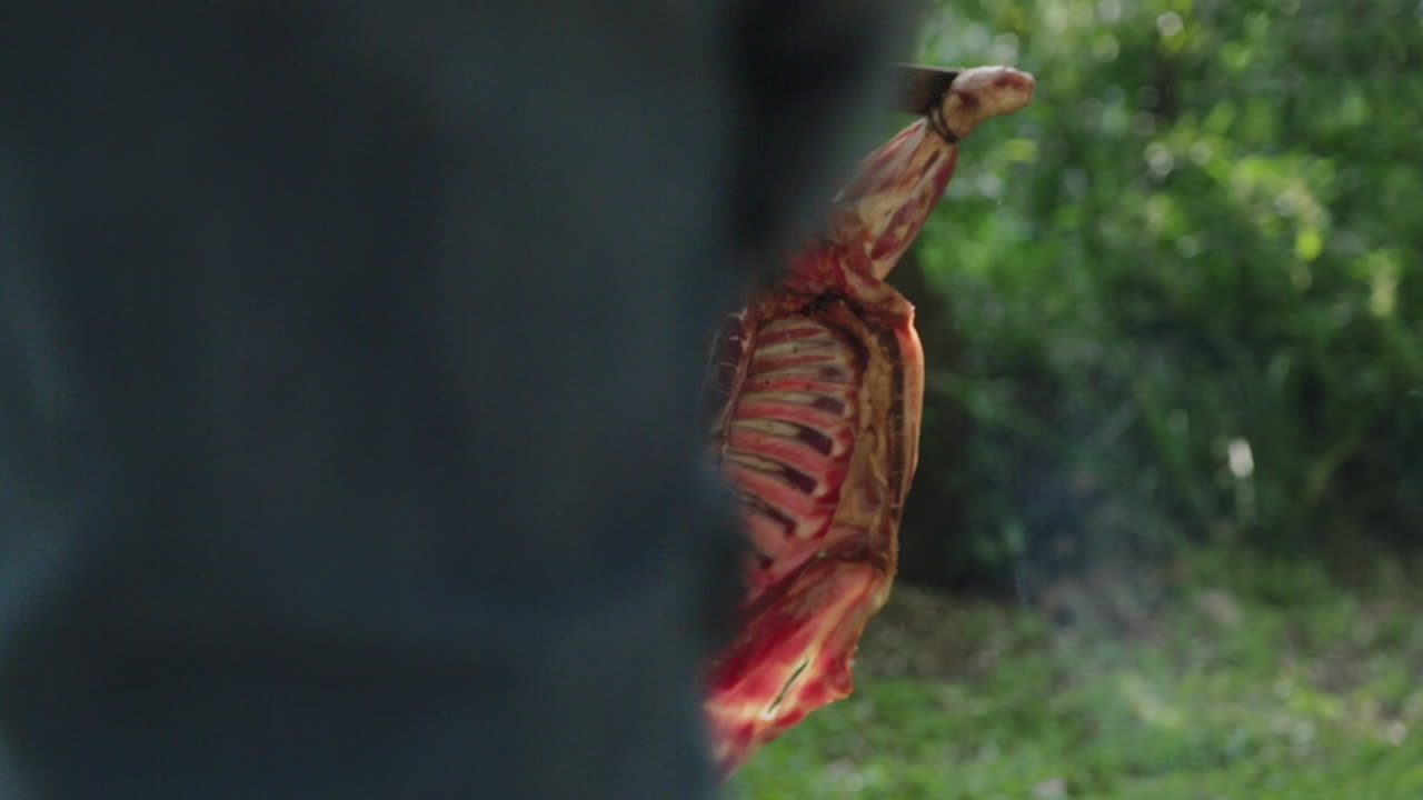 hombre comprobando el calor de la hoguera en carne de cordero en una cruz en el parque al aire libre