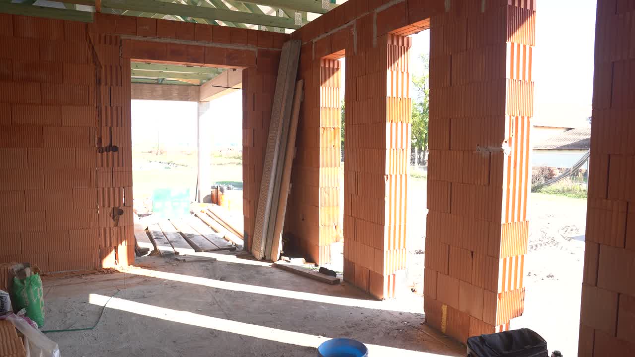 Sunlit unfinished brick house interior with open doorways and window openings