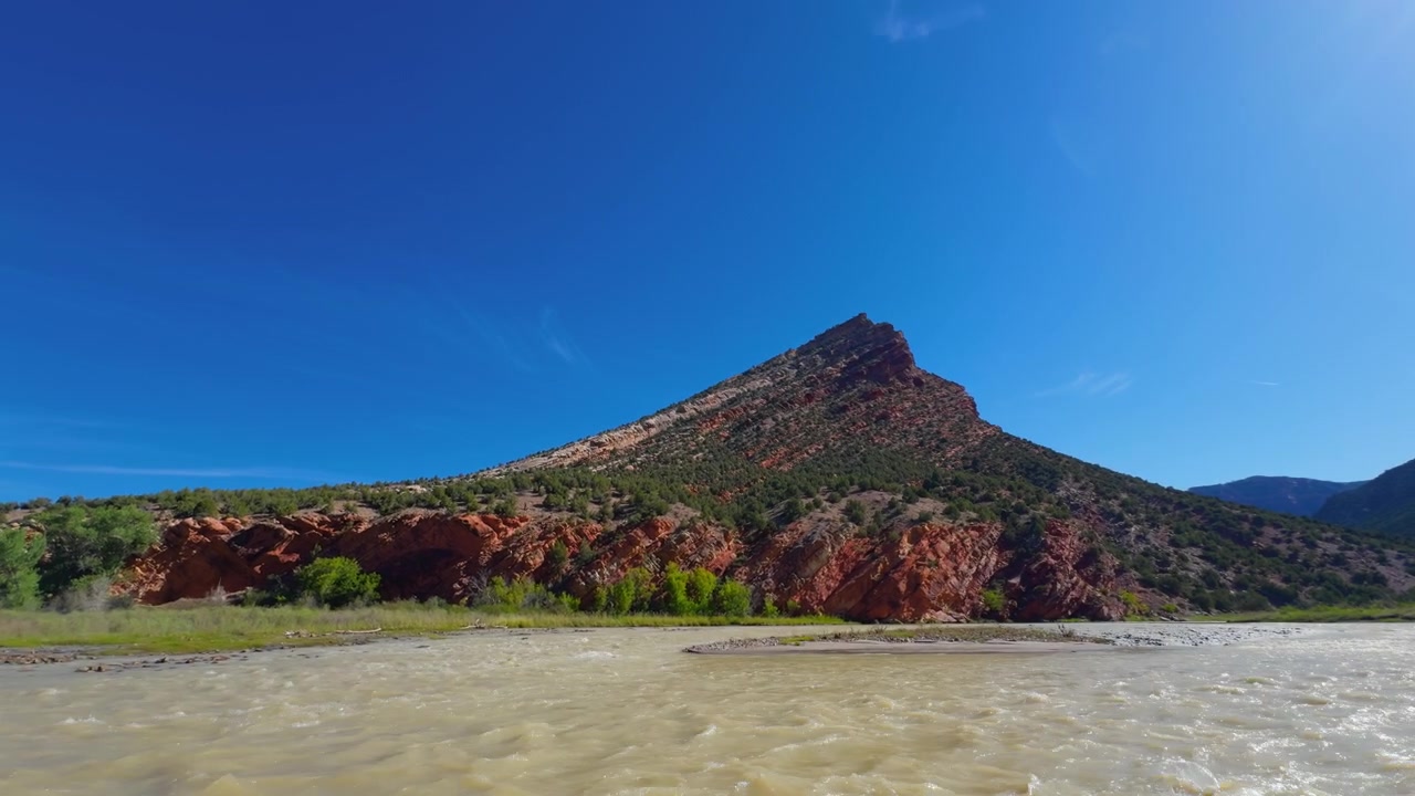 Un butte desertico isolato si erge sopra il fiume Yampa sotto cieli azzurri e limpidi, esperienza di pack rafting nel backcountry attraverso le rapide del fiume.