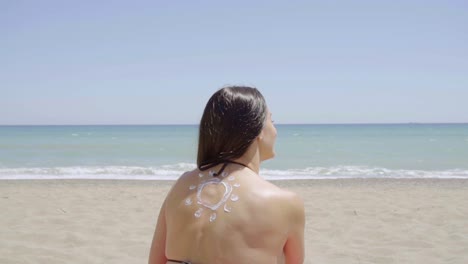 mujer joven con un protector solar en la espalda