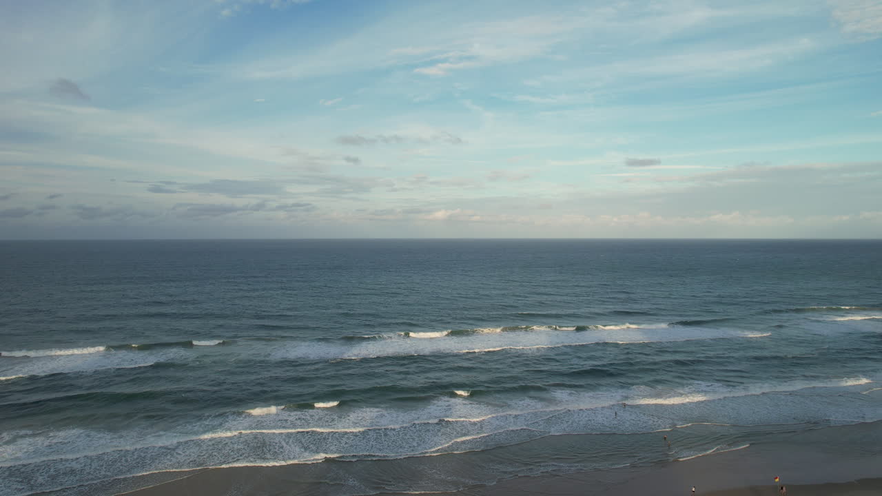 Beachgoers On Sandy Shore Of Surfers Paradise Beach With Waves Rolling In Slow Motion. Queensland, Australia. ascending drone shot