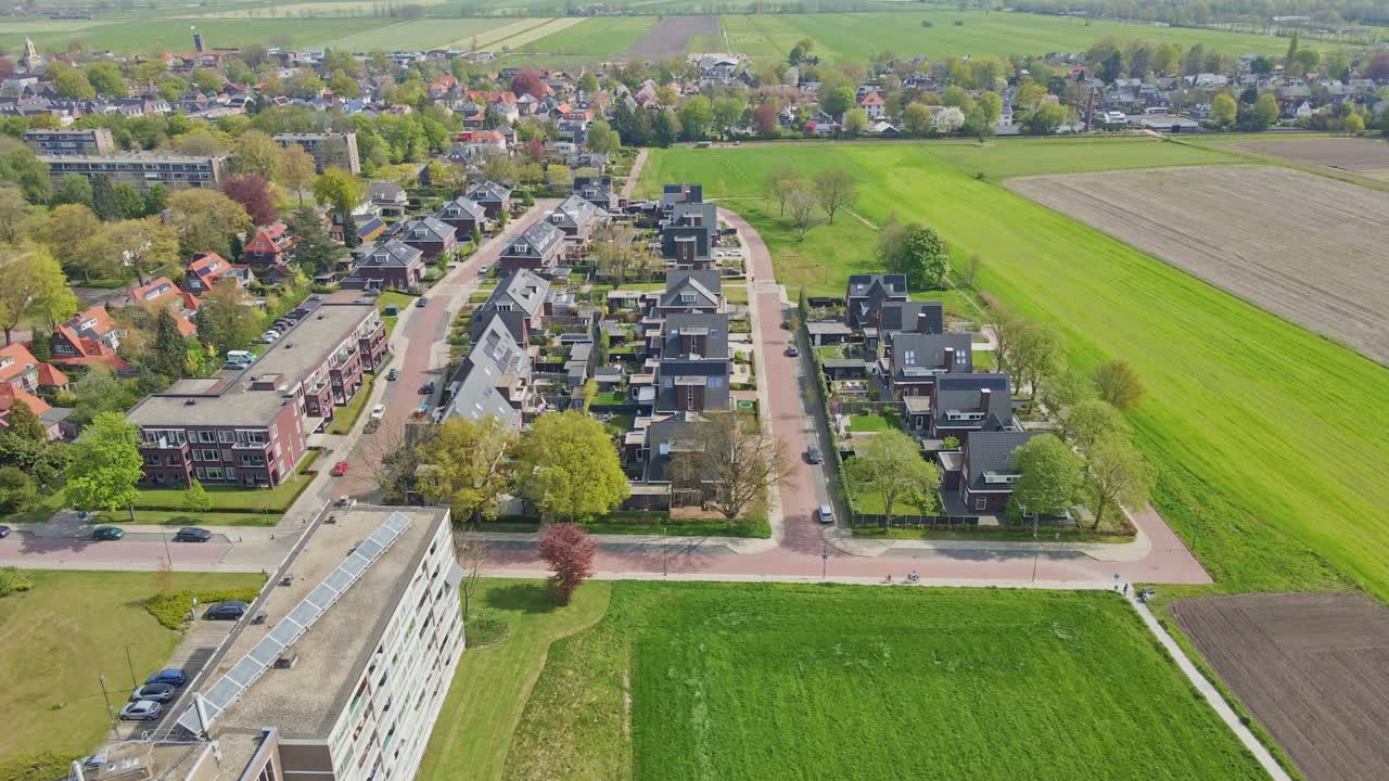 En drönare flyger förbi ett hyreshus mot ett modernt bostadsområde.