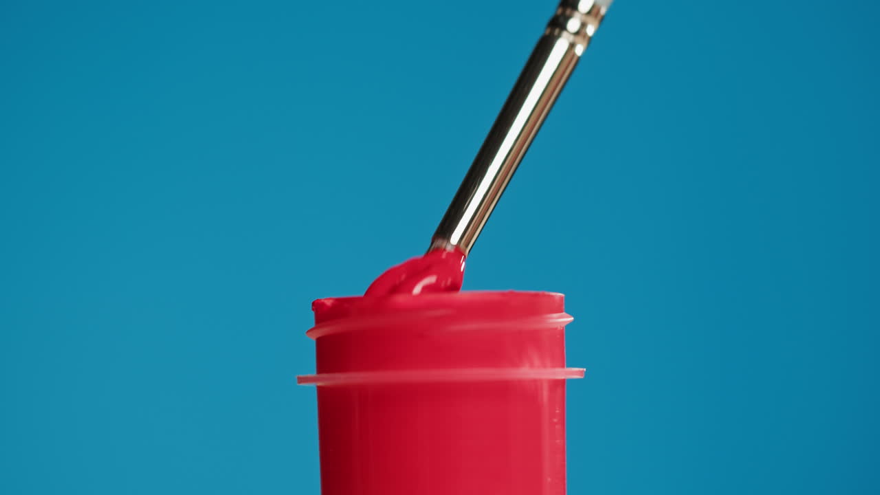 Pincel sumergiéndose en pintura roja con un fondo azul