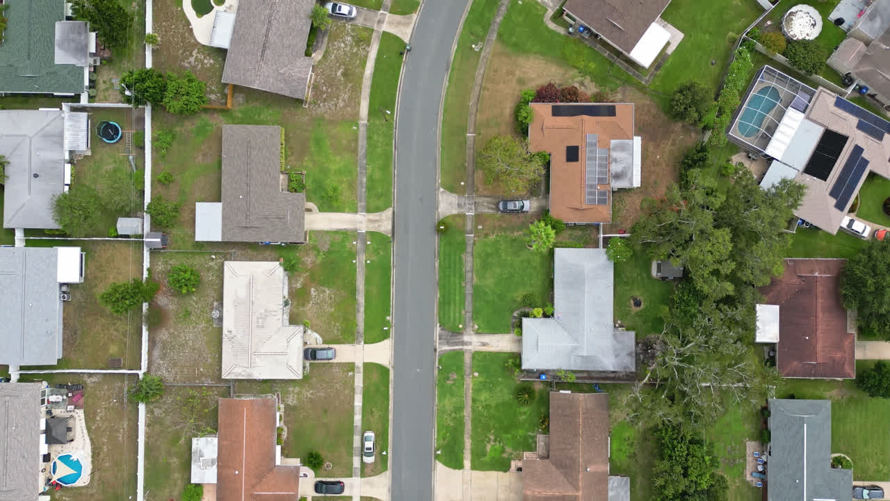 Top down aerial of suburban houses and backyards arranged in green residential blocks