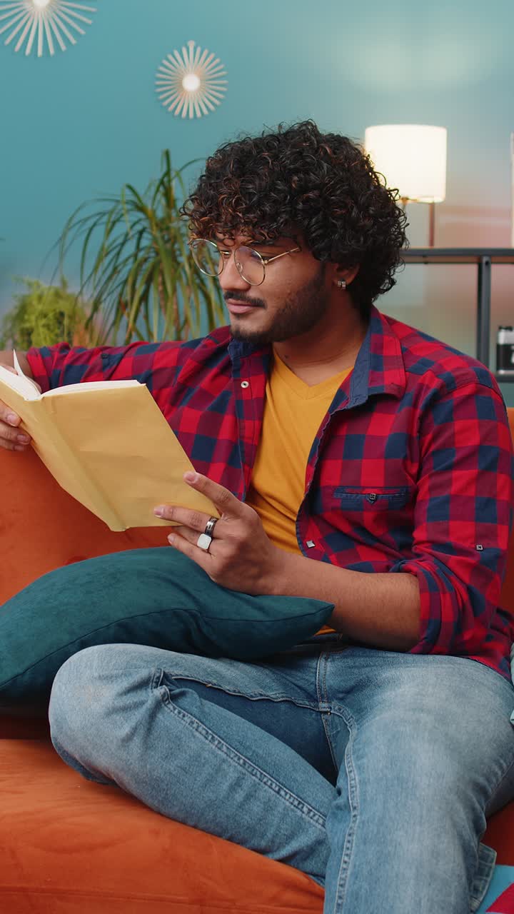 Un Indien lit un livre intéressant, tourne les pages, sourit, apprécie la littérature, se repose sur le canapé.