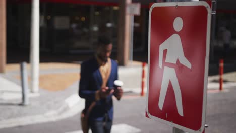 African-american-businessman-holding-coffee-using-smartphone-in-street