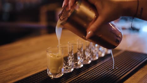 bartender filling up shot glasses with colorful drink