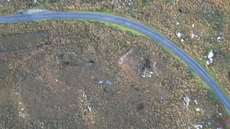 Bird-eye-aerial-of-natural-ground-surface-and-asphalt-road-leading-through-it,-location-Connemara,-a-region-of-immense-natural-beauty-in-Ireland