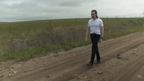 man walking on dirt road by expansive fields