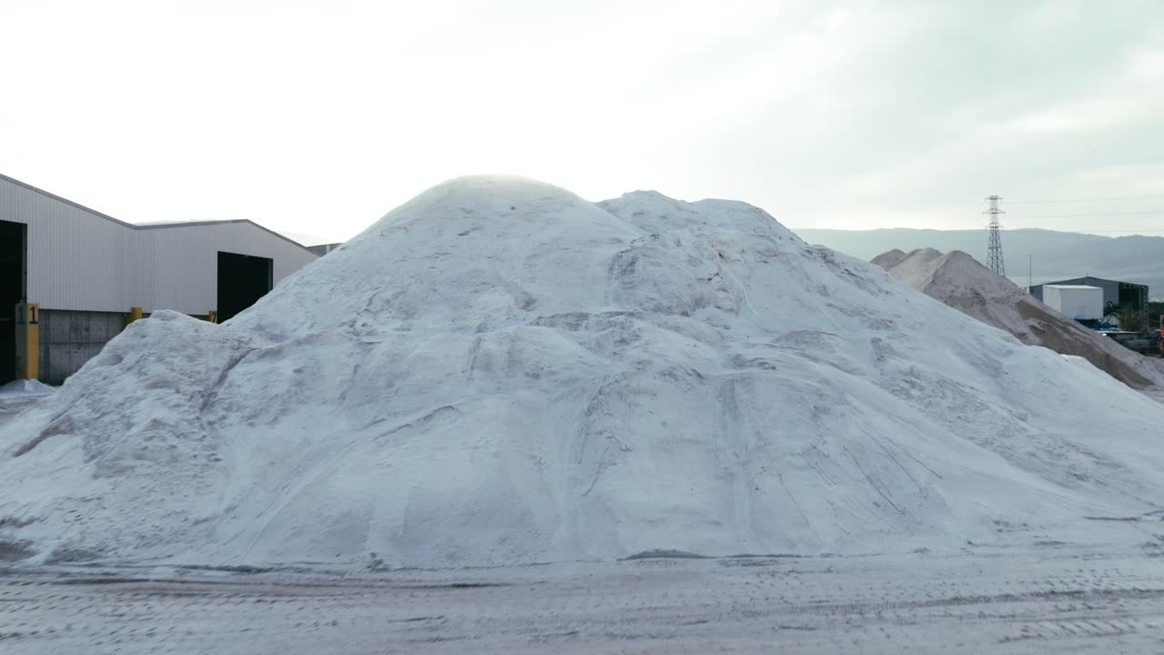 A large, industrial salt or mineral storage yard, with mounds of white material piled high under the soft sunlight.