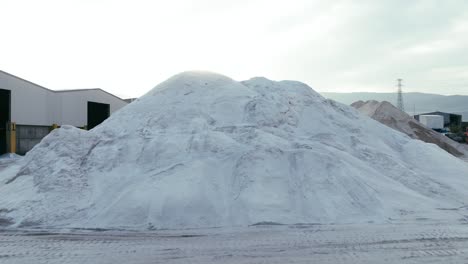 a large, industrial salt or mineral storage yard, with mounds of white material piled high under the soft sunlight.