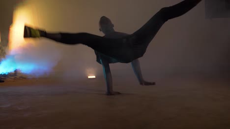 slow motion shot of african youth doing break dancing spins on his back in colorful blue smoke