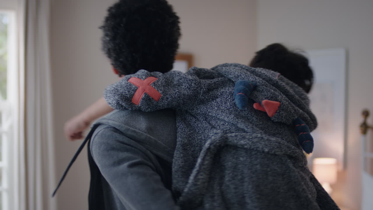 행복한 작은 소년은 아버지의 등으로 뛰어들어 아버지와 함께 놀고 집에서 아들과 함께 장난스러운 게임을 즐기고 있습니다.