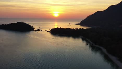 tranquil sunset landscape aerial shot capturing pulau burau islet and beautiful orange glowing sun setting below the horizon at pantai kok beach, island shore bounded by strait of malacca, langkawi