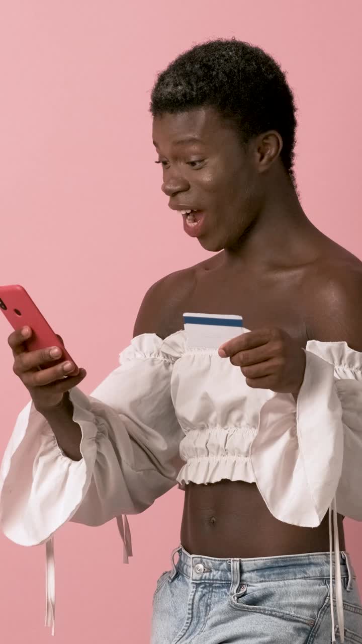 African transgender person smiling while using mobile phone and credit card.