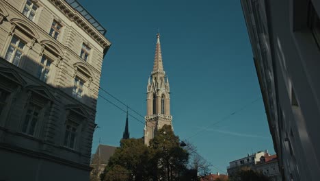 aguja de la iglesia neogótica enmarcada por edificios históricos bajo un cielo despejado en viena