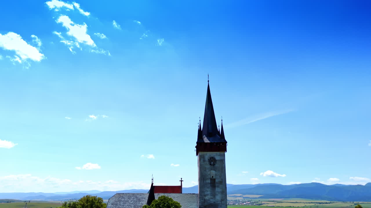 Approaching the spire of the old church. Vast beautiful valley surrounded by the mountain range at backdrop.