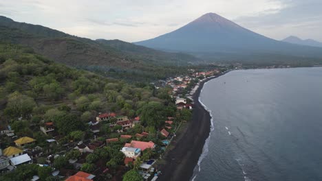 drone flying over a small coastal village with black sand beaches and volcano in the background