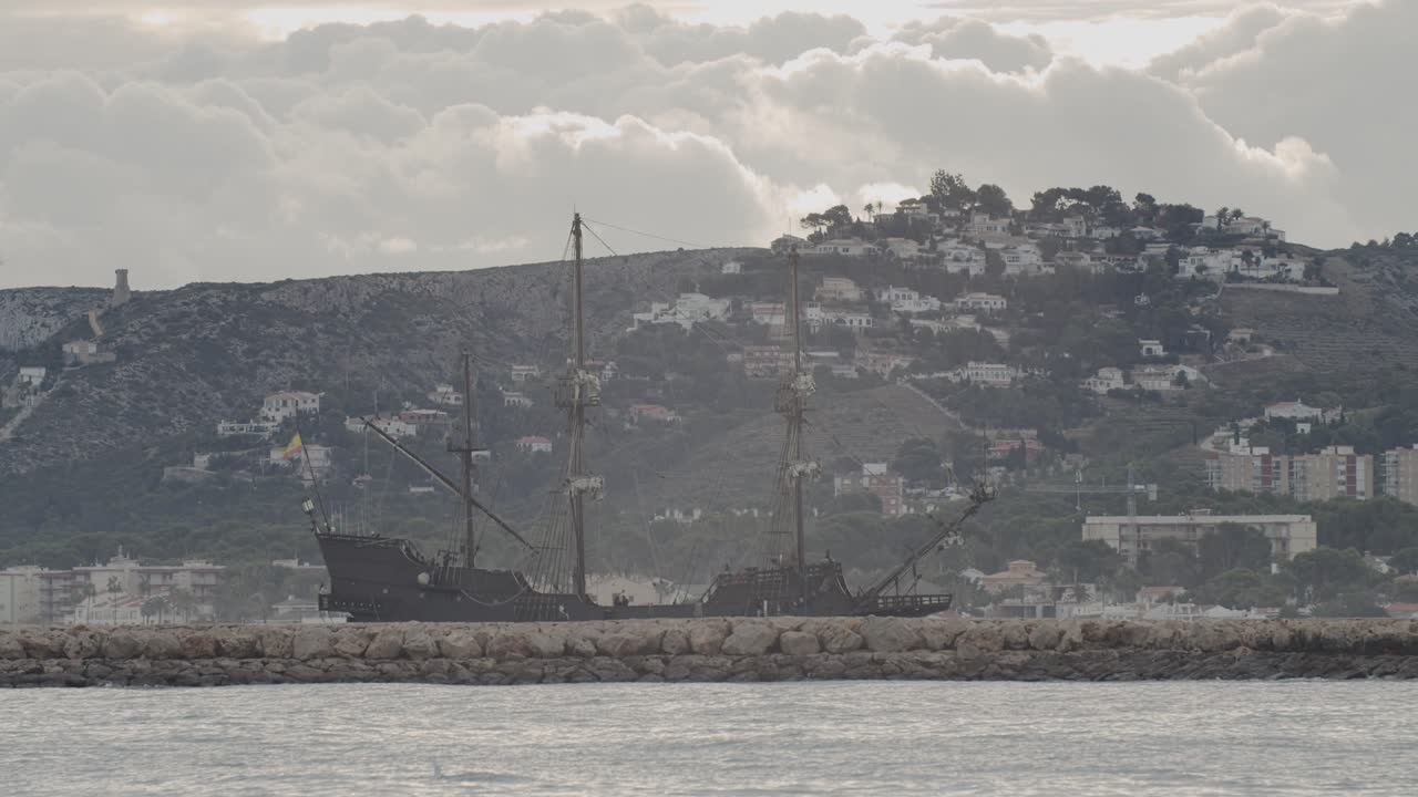 16세기 갤리온 안달루시아 복제선은 산과 집들이 배경에 있는 방파제 뒤에서 일출 때 아름다운 흐린 날 항구에 도착했습니다.