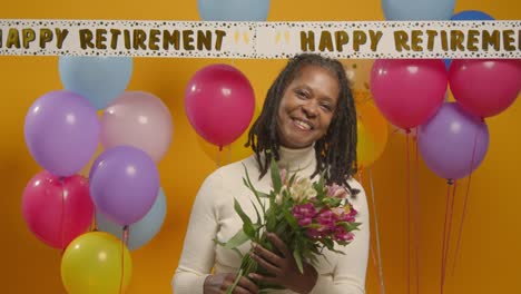 Studio-Portrait-Of-Woman-At-Retirement-Party-Holding-Bunch-Of-Flowers-Celebrating-With-Balloons-1