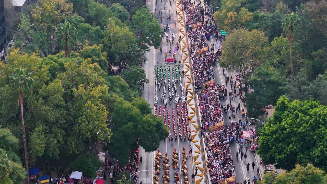 Ascending aerial shot of the Day of the Dead parade held on Paseo de la Reforma, with a bird's-eye view of the parade ending with a direct shot of Chapultepec Castle in Mexico City