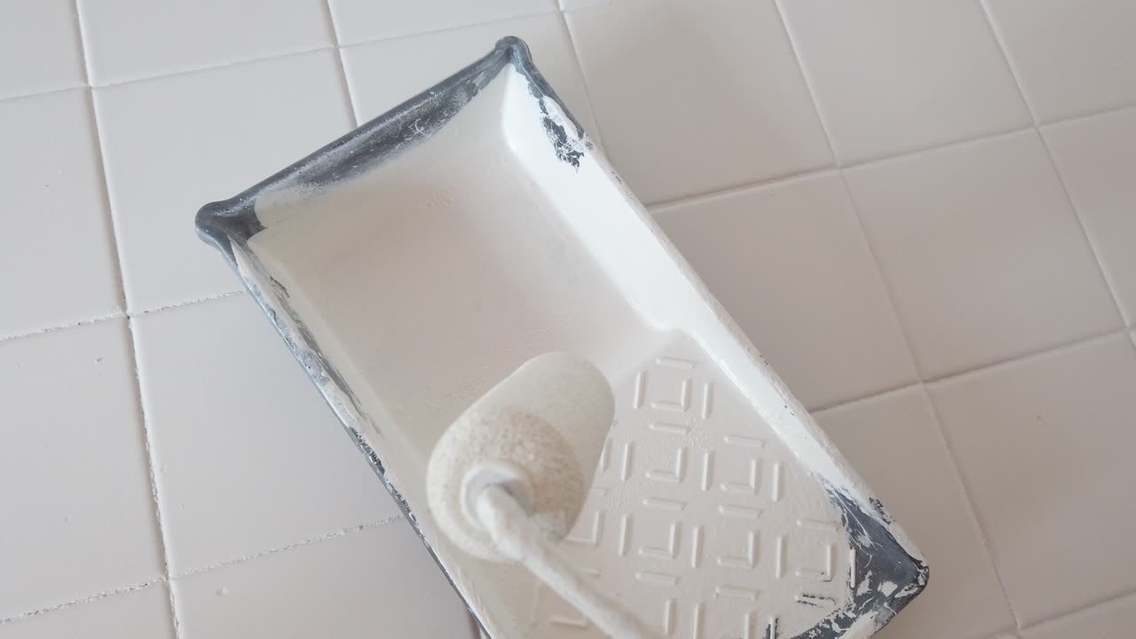 Close up of paint roller applying white paint on tiled wall during home renovation