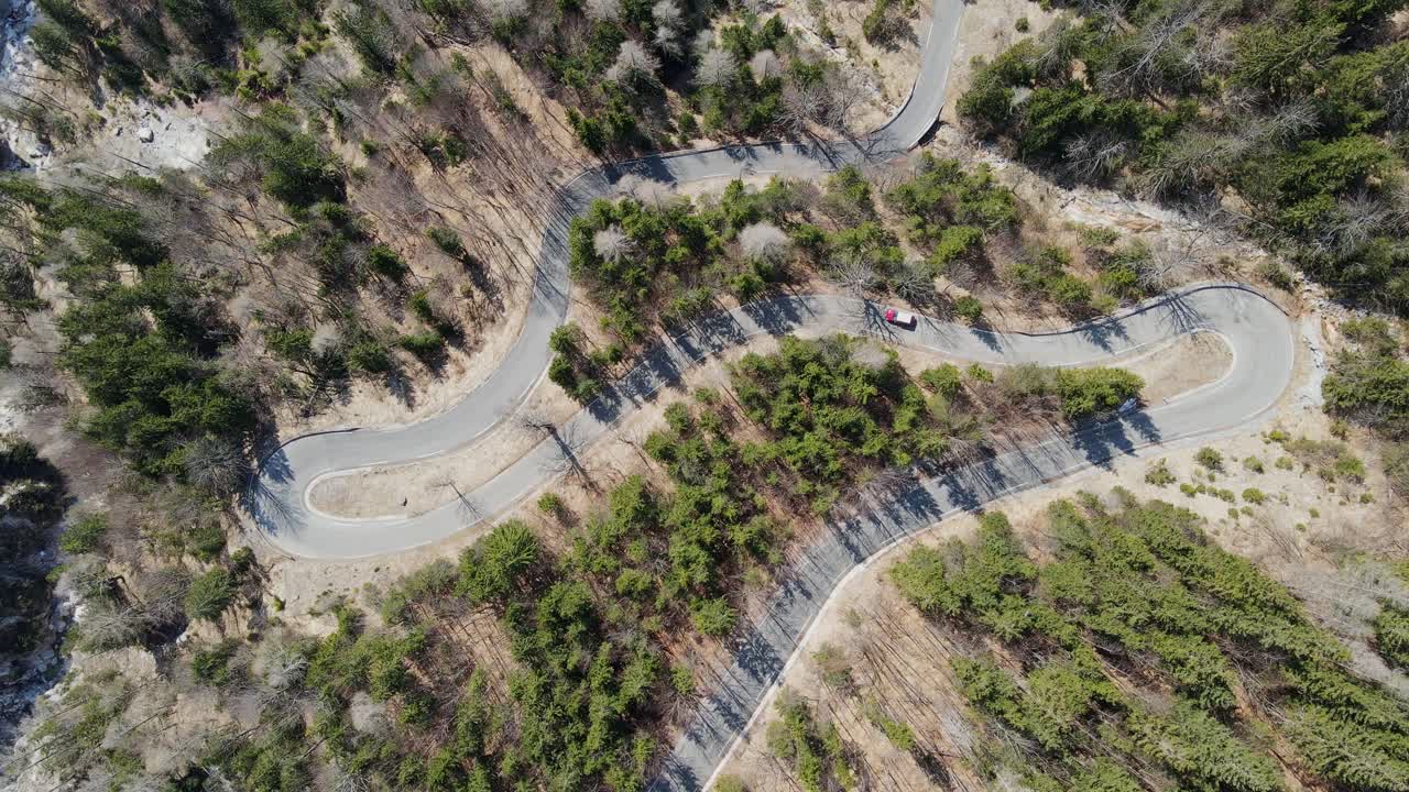 Aerial shot capturing the curves of peaceful mountain road through dense forest