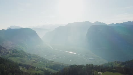 an aerial shot revealing a vast and breathtaking south tyrolean valley surrounded by towering mountains and a glowing horizon.