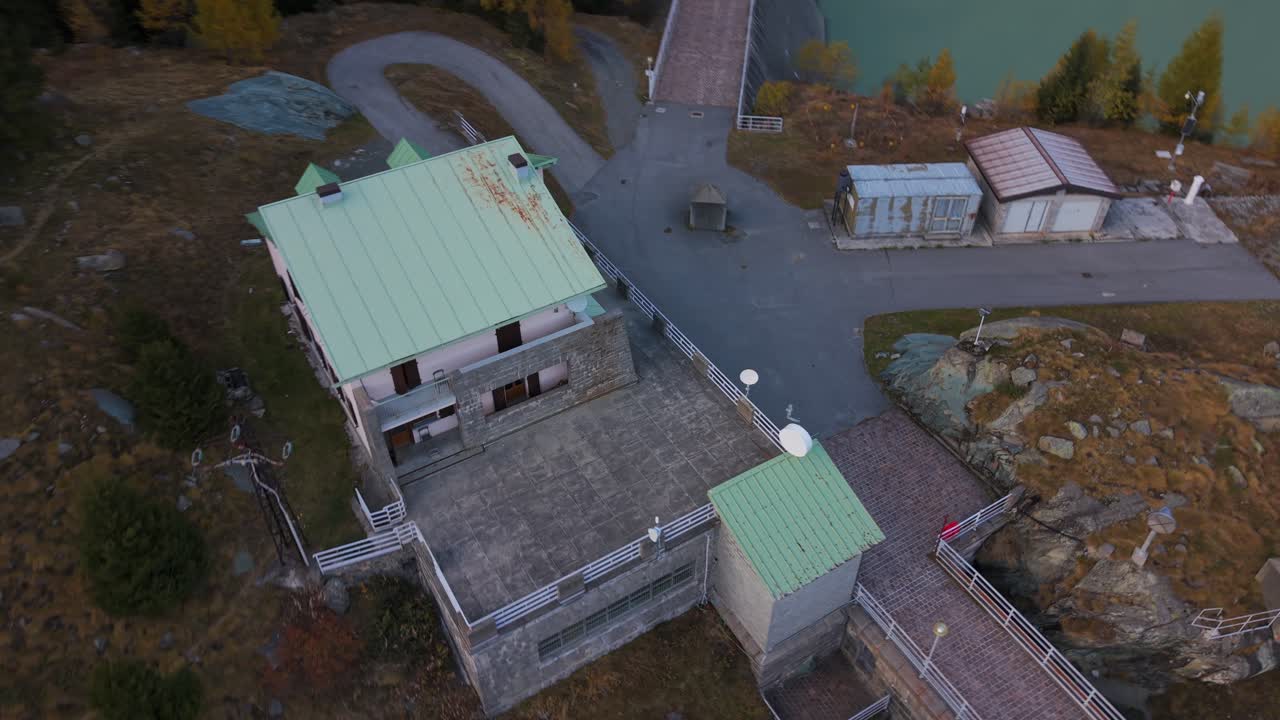 Aerial view of Valmalenco Diga Campo Moro dam and a building with a green roof in Lombardy Italy A reservoir and autumnal trees in the surrounding landscape