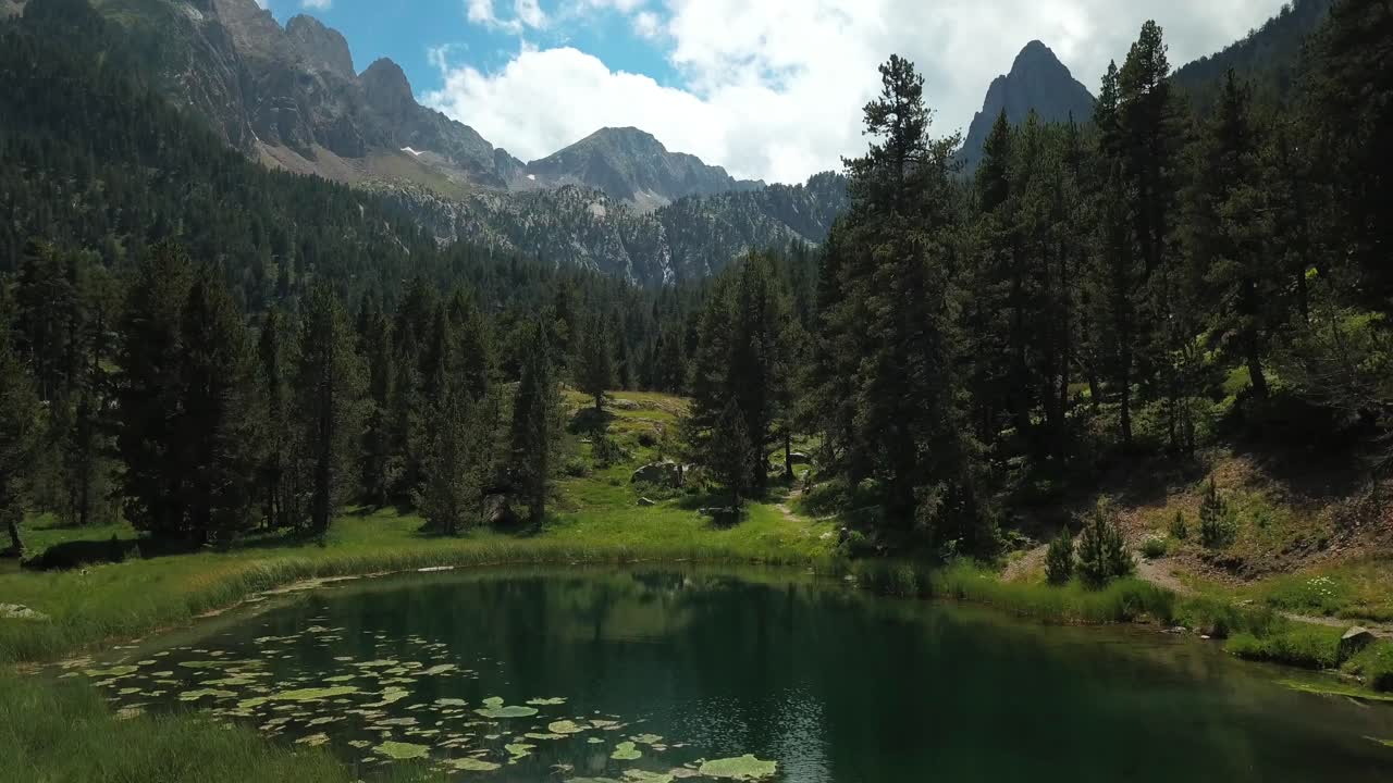 Aerial horizontal 4K footage of a lake in a green natural environment with mountains in the Spanish Pyrenees