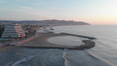 un dron captura una tranquila ciudad costera mientras las tranquilas olas del océano chocan contra numerosos pilares de piedra que se adentran en el agua