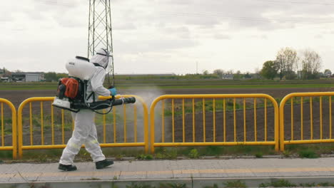 man in the protective suit disinfecting bus stop with a spray gun to prevent coronavirus spread. spraying the gate