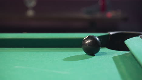 black billiard ball rolls towards pool pocket after being struck by white cue ball on green felt table. focus on precision, impact, and movement in competitive gameplay setting with dramatic lighting