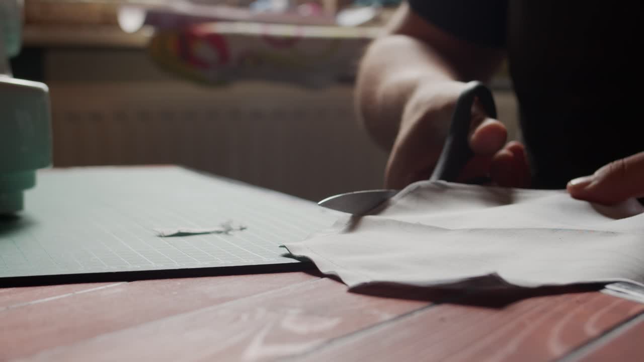 Slow motion cutting of fabric with scissors on a table backlit by natural light