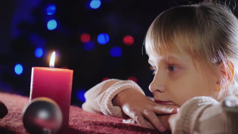 portrait of a child looks at a candle makes a wish on christmas eve