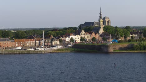 Beautiful-wide-aerial-shot-of-a-kite-surfer-zipping-along-the-Dutch-shore-in-the-providence-of-Zeeland-with-the-old-town-of-Veere-in-the-background