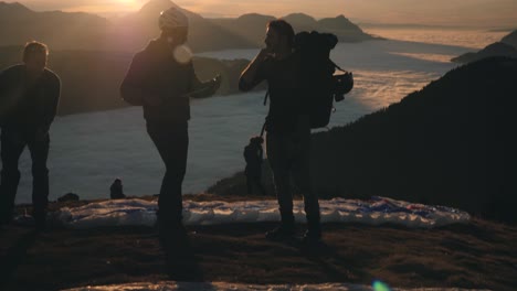 paragliding - group of people giving instructions and preparing equipment on hill before take-off on mountain at sunset. - tilt up