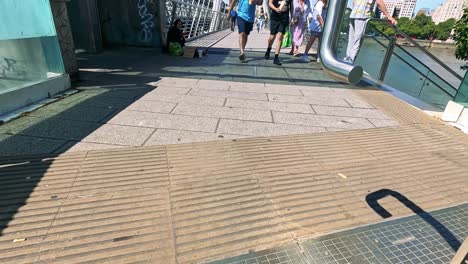 people walking past a beggar on bridge