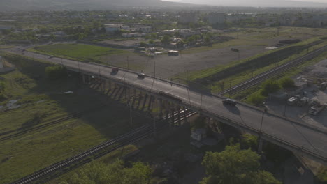 Aerial-tracking-shot-of-fast-moving-cars-driving-over-a-railway-bridge