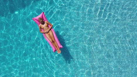Overhead-Drohnenaufnahme-Einer-Frau-Im-Sommerurlaub,-Die-Auf-Einer-Aufblasbaren-Luftmatratze-Im-Schwimmbad-Schwimmt